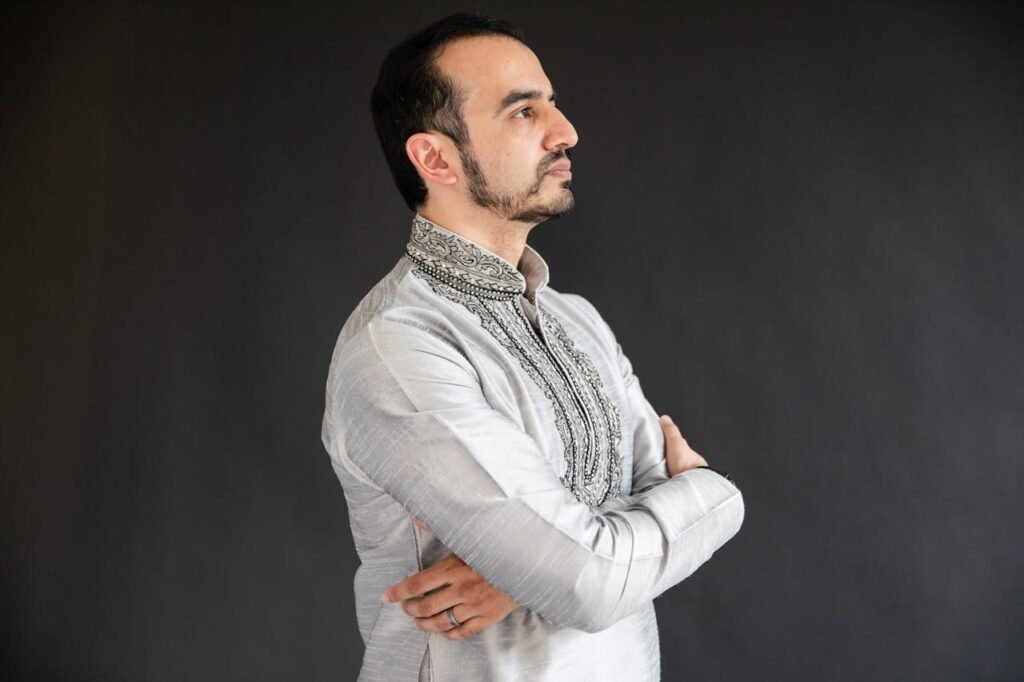 Home Middle Eastern man in traditional attire poses confidently against a dark background.