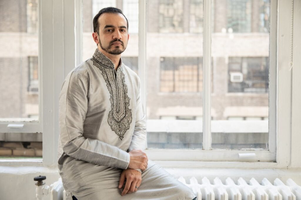 Home A man in traditional clothing sits by a window, capturing a blend of cultural and modern design.